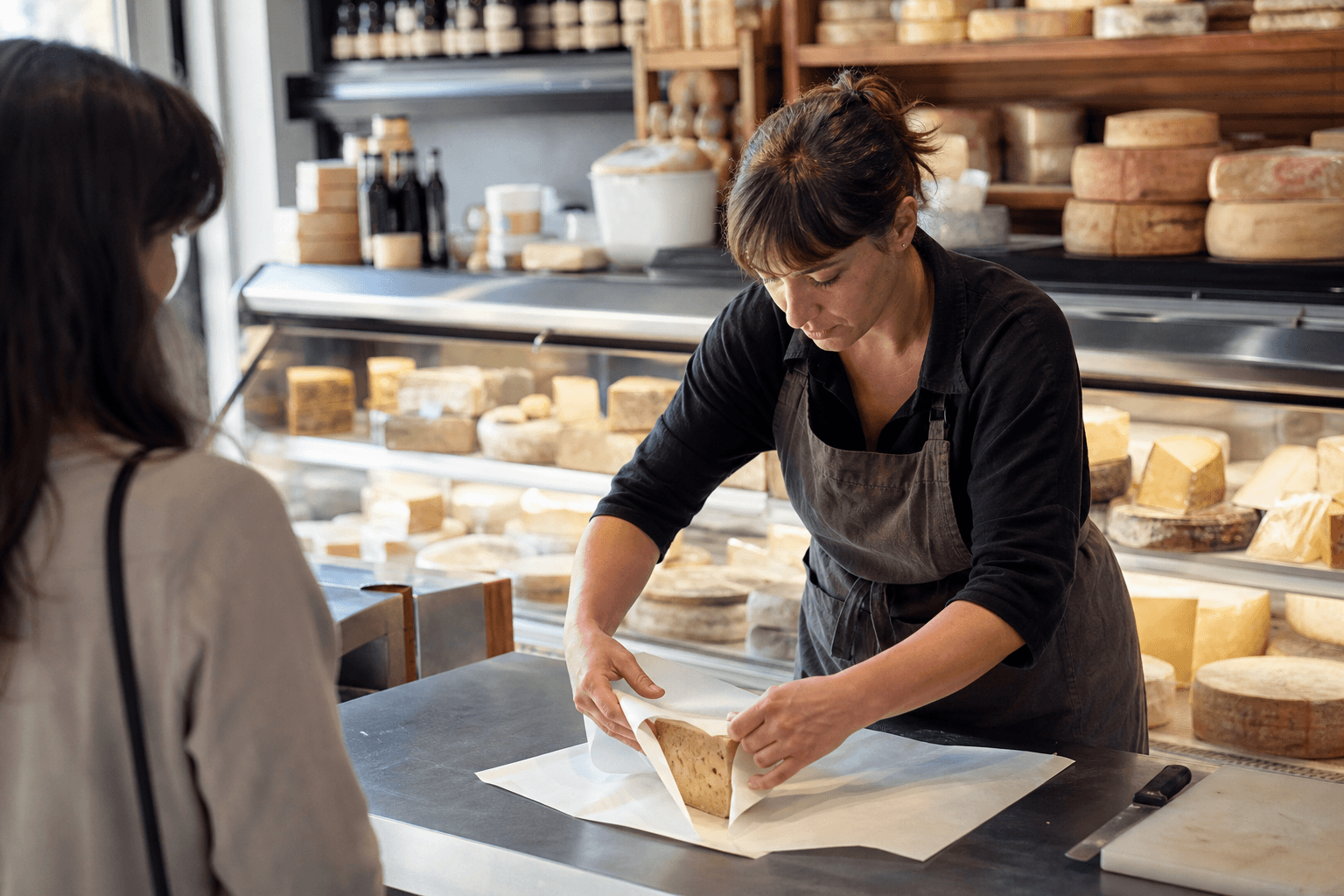 Cheesemonger arranging wheels while a customer waits